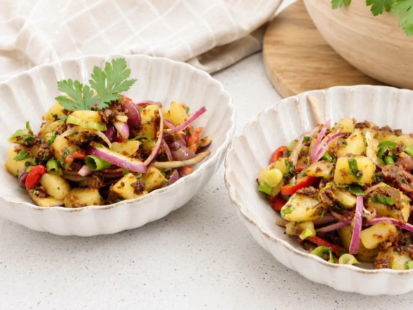 Potetsalat med soltørkede tomater, poteter, grønnsaker, kalamataoliven og persille, servert i skåler.