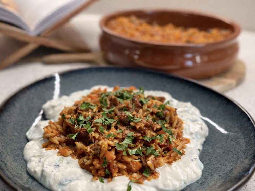 Gresk giouvetsi med storfekjøtt og orzo, servert på kremet agurksalat med frisk persille på toppen.