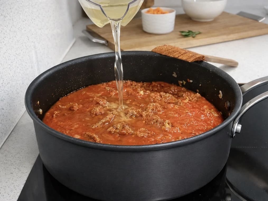 Tomatsaus med storfekjøtt i panne mens grønnsakskraft helles i blandingen.