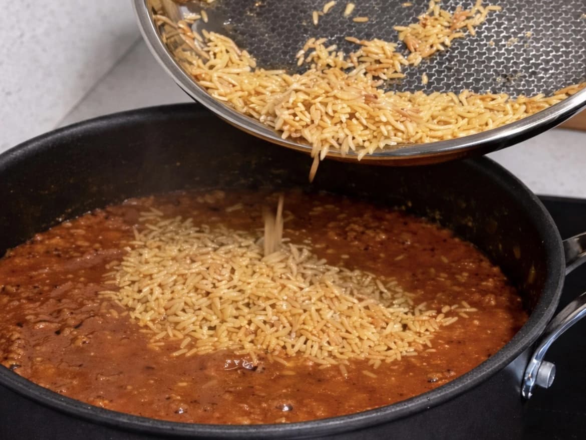 Ristet orzo helles fra en stekepanne over i tomatsausen med storfekjøtt.