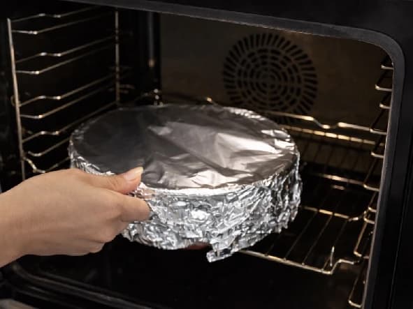 Ildfast form med giouvetsi dekket med aluminiumsfolie settes inn i ovnen for steking.
