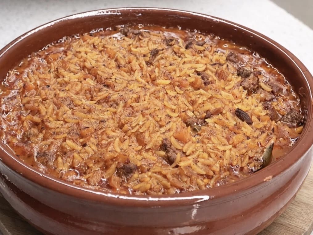 Ferdigbakt gresk giouvetsi med mørt storfekjøtt og orzo i fyldig tomatsaus, servert i en brun ildfast leirform.