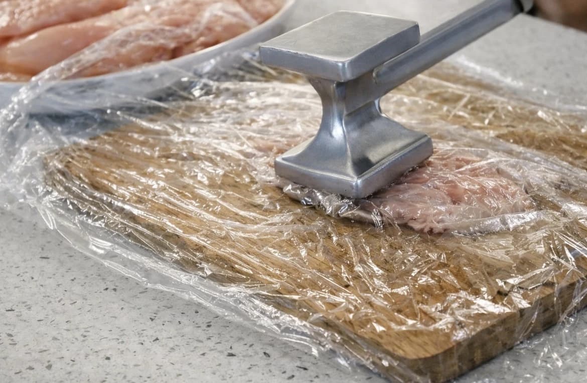 Kyllingfilet mellom plastfolie bankes flat med en kjøtthammer før steking.
