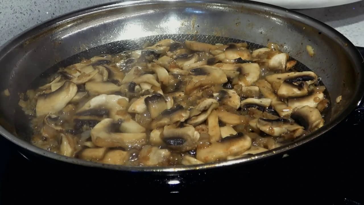 Sjampinjong og finhakket løk stekes i panne for å lage en smakfull soppsaus.