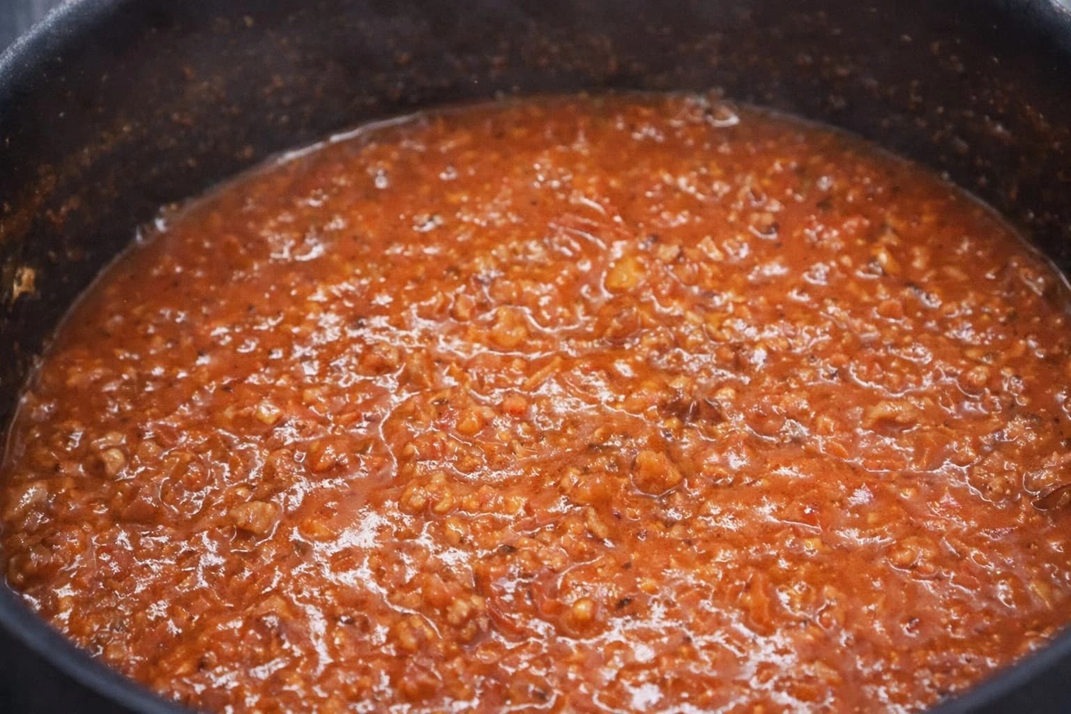 Bolognese-saus med kjøttdeig og tomater småkoker i en panne til den blir fyldig og smakfull.