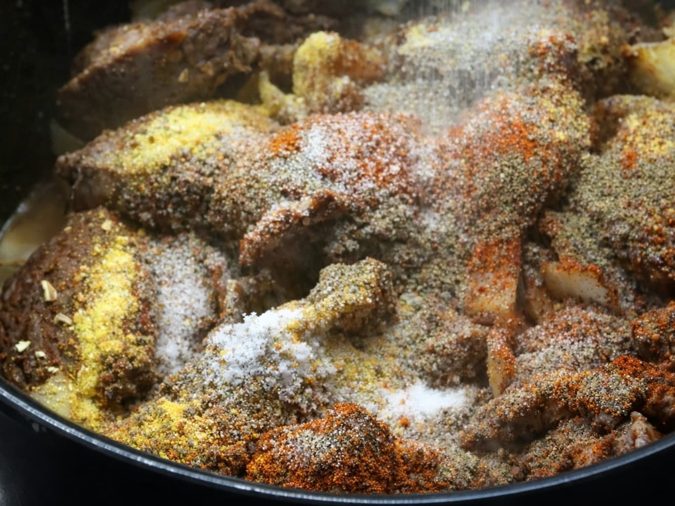 Krydderbelagte kjøttstykker i panne, med hvitt salt og gule urter strødd over.