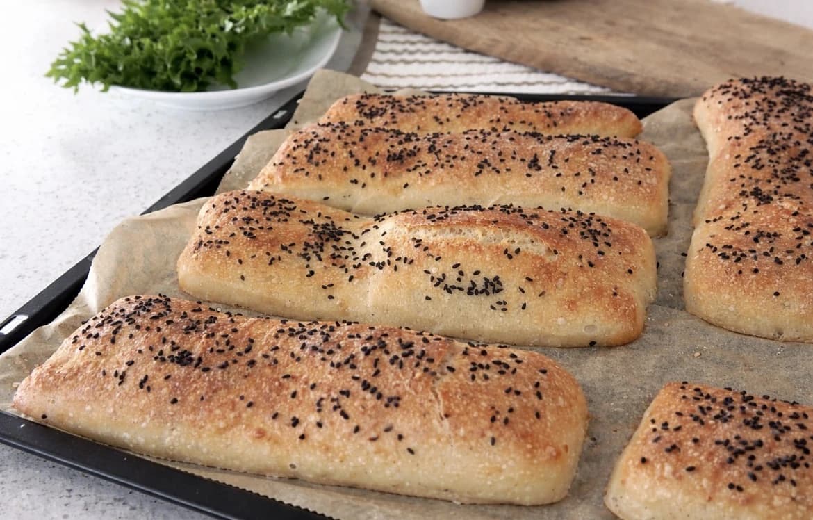 Hjemmelagde sandwichbrød i ciabatta-stil, gyllenbrune og toppet med svarte frø.