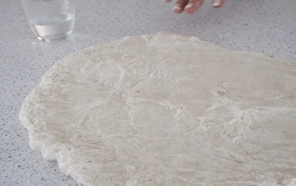 Ciabattadeigen trykkes forsiktig ut til et stort rektangel med fuktige hender.
