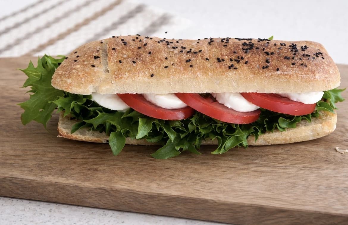 Hjemmelaget ciabatta-sandwich med mozzarella, tomat, grønne salatblader og sprøtt brød med svarte frø.