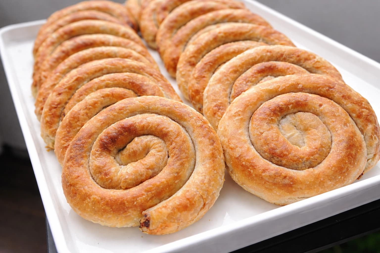 Hjemmelaget burek med kjøttdeig, rullet i spiraler og servert på et hvitt fat med gyllen, sprø overflate.