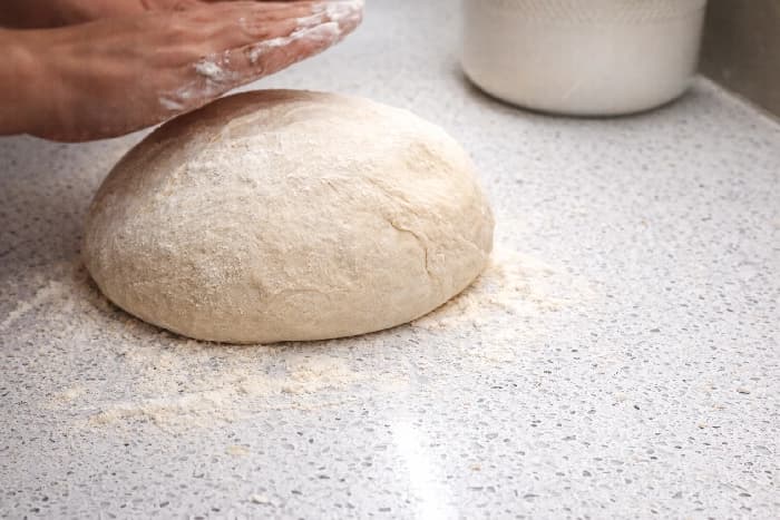 Burekdeigen formes til en stor, rund ball på en melet benkeplate før den deles i mindre emner.
