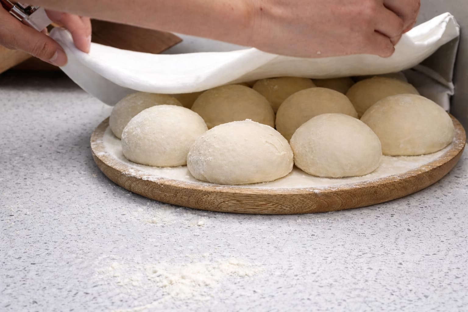 Små deigballer til hjemmelaget burek hviler tildekket med et kjøkkenhåndkle på en melet trefjøl.