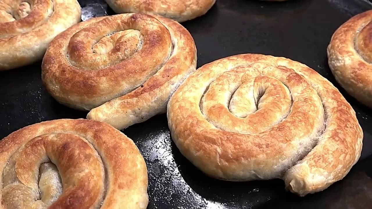 Nystekte burek med kjøttdeig, formet som spiraler med gyllen og sprø skorpe på et stekebrett.