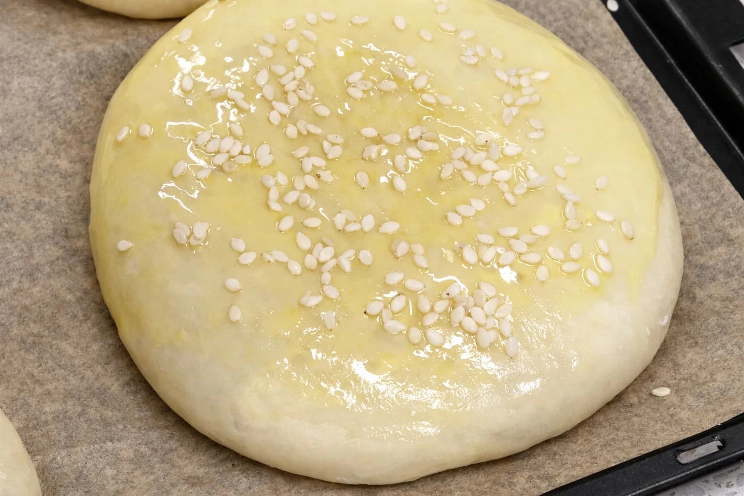 Hamburgerbrød penslet med sammenvispet egg og drysset med sesamfrø før steking.