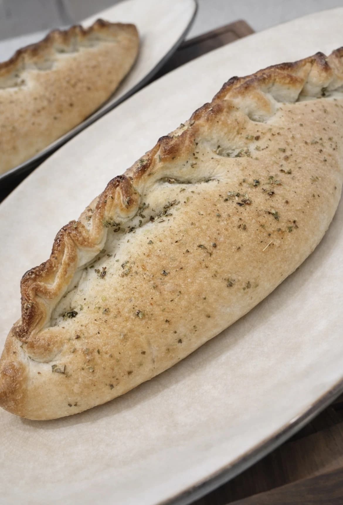Nystekt innbakt pizza med gyllen skorpe og oregano, servert på et fat.