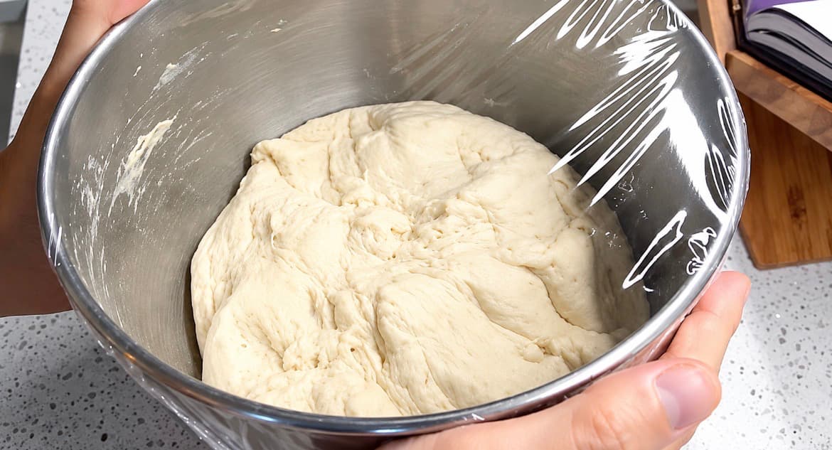 Pizzadeig i en bolle dekket med plastfolie, klar til heving.