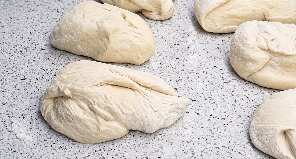 Pizzadeigen deles opp i mindre emner på en melet arbeidsbenk.