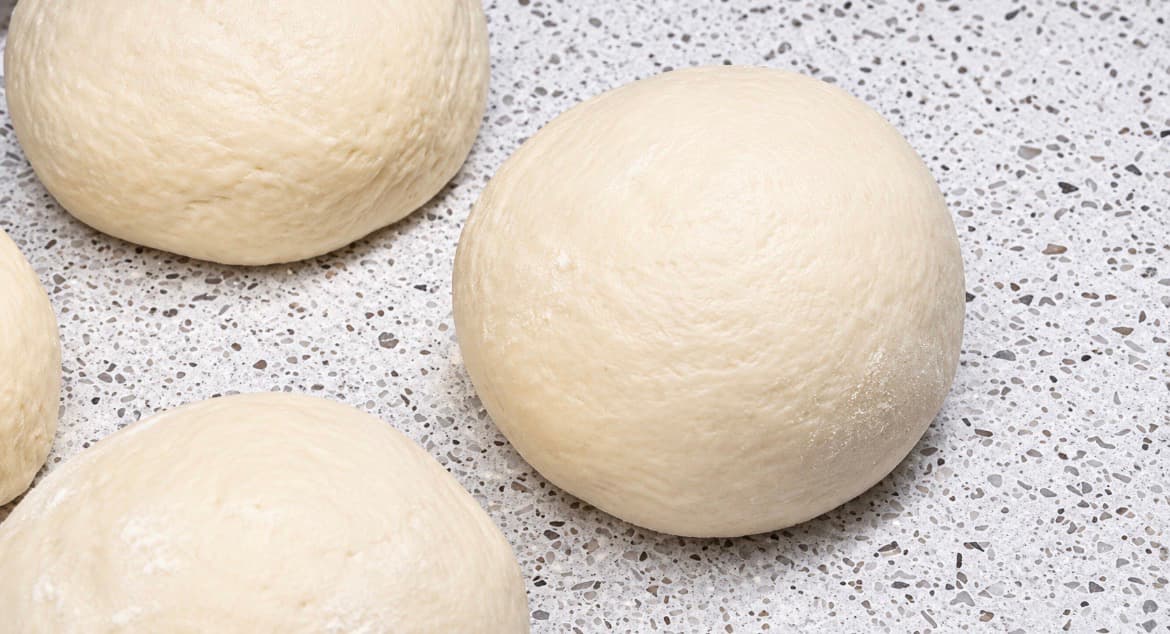 Deigemner formes til glatte, runde boller før de kjevles ut til innbakt pizza.
