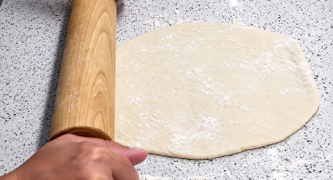 Pizzadeig kjevles ut til en avlang form på en melet arbeidsbenk.