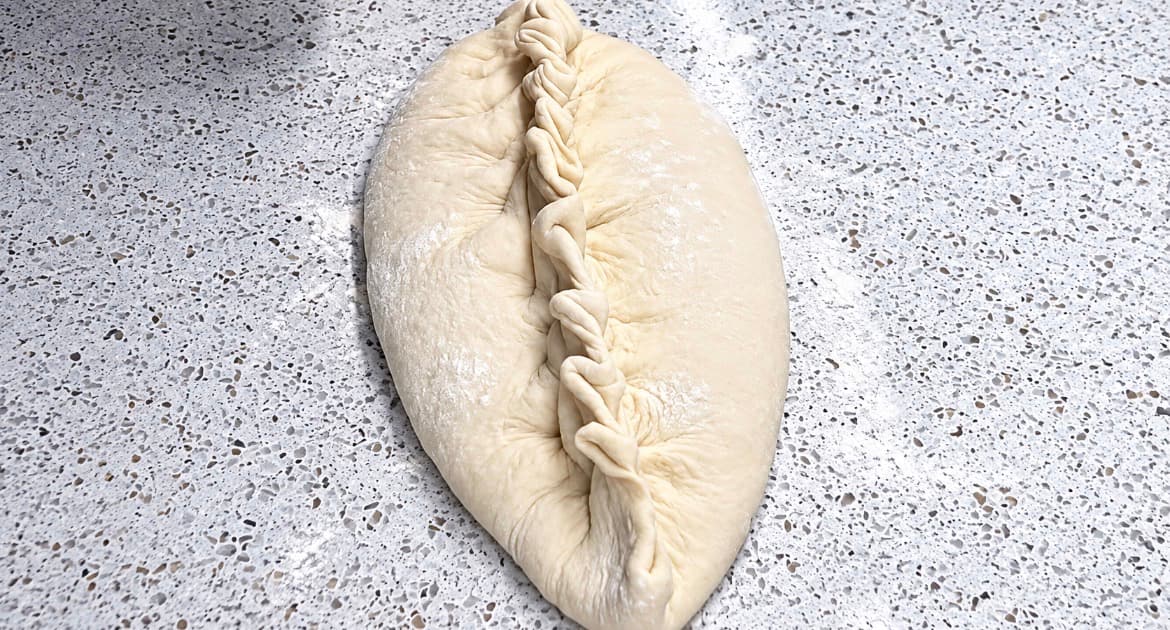 Innbakt pizza formes ved å flette deigkantene sammen over fyllet for å lukke pizzaen godt.