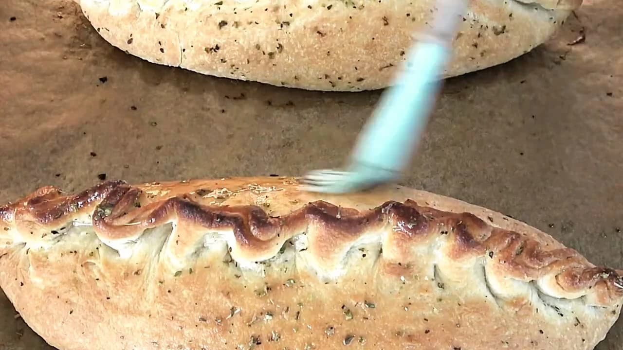 Innbakt pizza pensles med olivenolje og oregano etter steking for ekstra smak og glans.